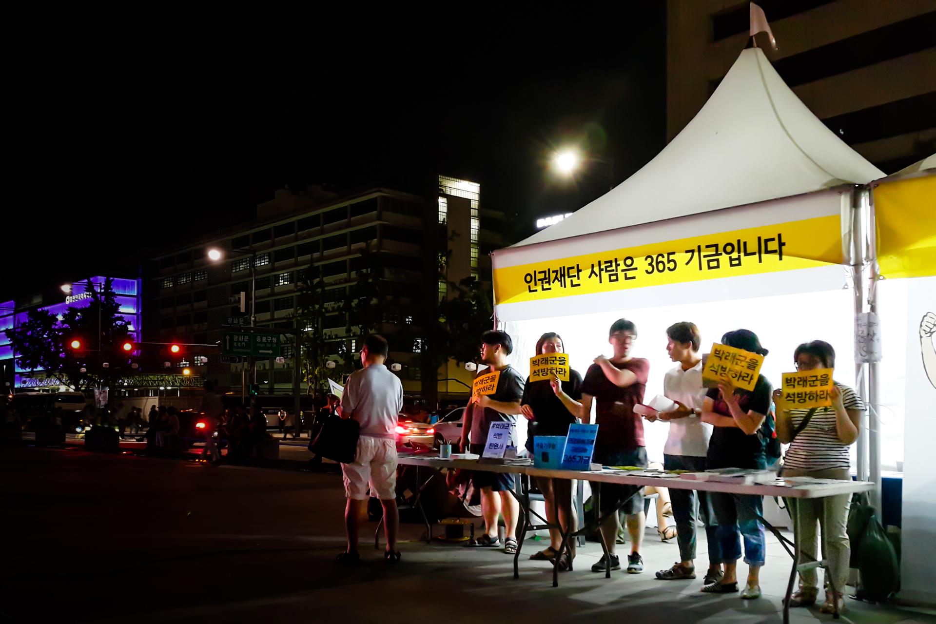 어두운 거리에서 5,6명이 박래군을 석방하라라는 손팻말을 들고 부스에 서 있다.