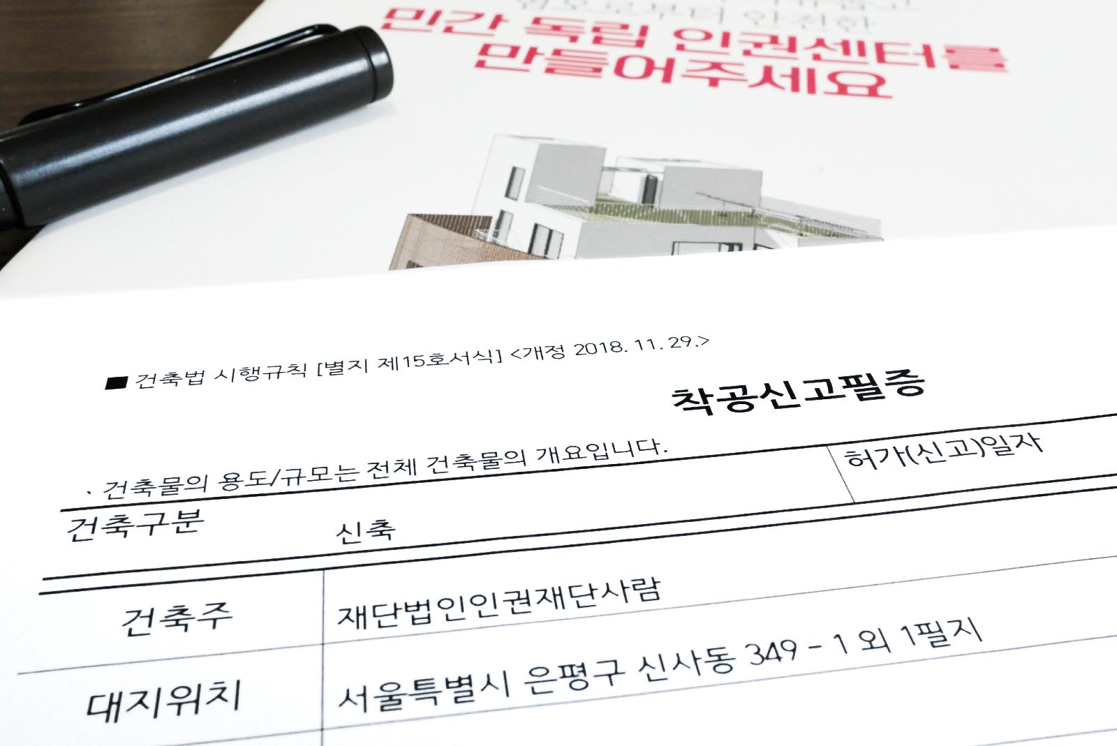 착공신고필증이라고 쓰인 증서가 어두운 배경의 바닥에 놓여있다.