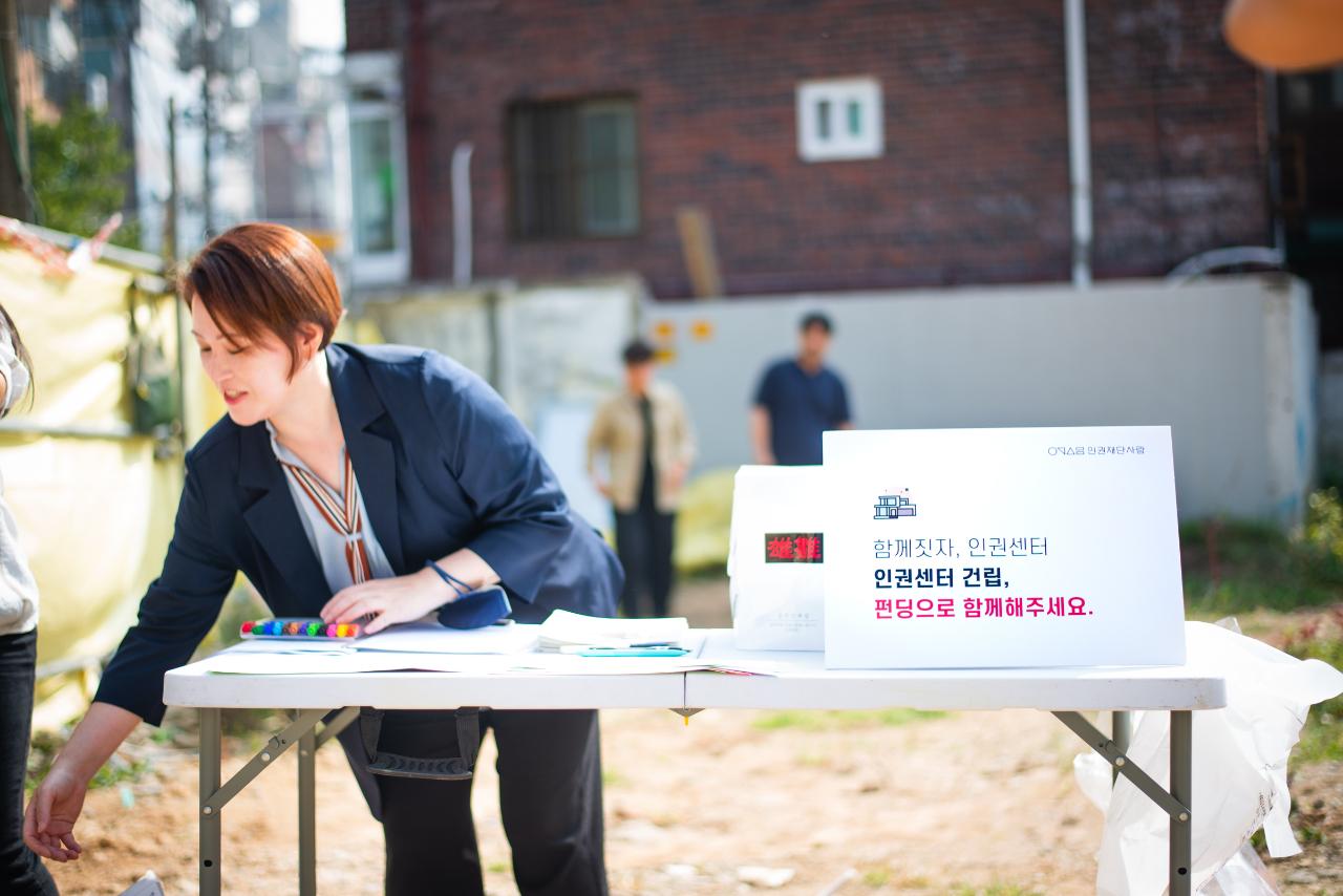 한 여성이 테이블 아래에서 무언가를 꺼내려고 허리를 숙이고 있다.